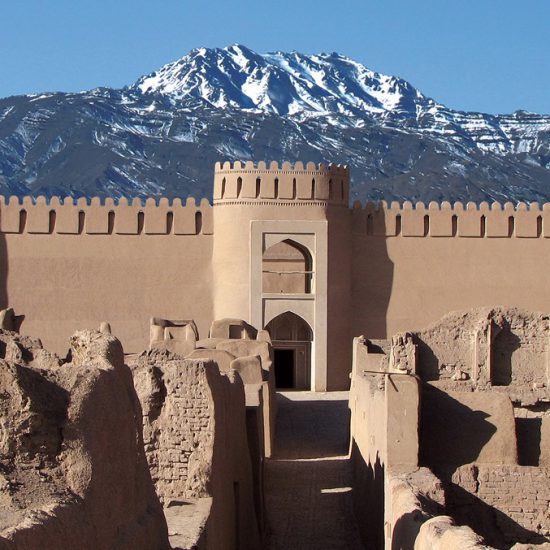 a facade view of Rayen Castle with snowy mountains behind it, Kerman, Iran