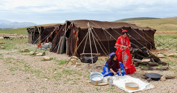 nomadic women wearing local clothes,baking bread near their tent, churn Mashk is behind them, nomadic lifestyle,Iran